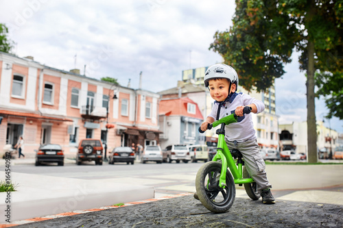 Little boy kid in helmet ride a bike in city park. Cheerful child outdoor.