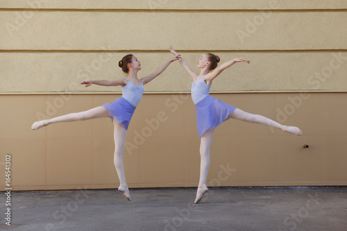 Ballet dancers dancing on street. Young ballerinas jump on yellow background full length