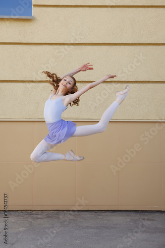 Fototapeta Naklejka Na Ścianę i Meble -  Ballet dancer dancing on street. Young ballerina jump on yellow background full length