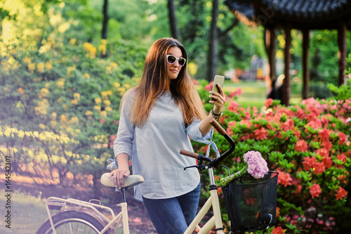 A woman with city bicycle in a summer outdoor park.