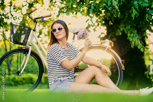 Portrait of brunette female sits on a lawn in a sunny park.