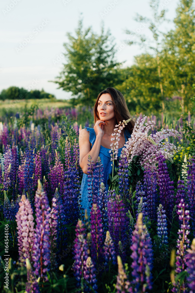 Beautiful woman dressed in a dress in flowers lupines at sunset Beautiful woman dressed in a dress in flowers lupines at sunset