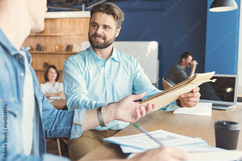 Happy young guy cooperating with colleague in office