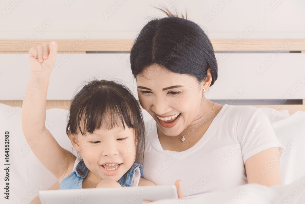 Asian women and child are having fun and happy together while using a tablet on the bed in the bedroom.Concept of family using technology Asian women and child are having fun and happy together while using a tablet on the bed in the bedroom.Concept of family using technology
