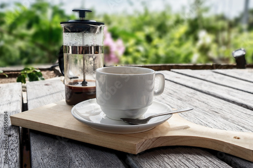 French press coffee maker and coffee cup studio lit on table with nature background photo