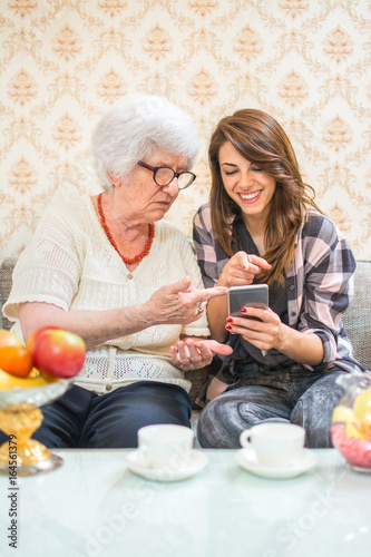 Grandmother and granddaughter commenting social media feeds on smart phone.
