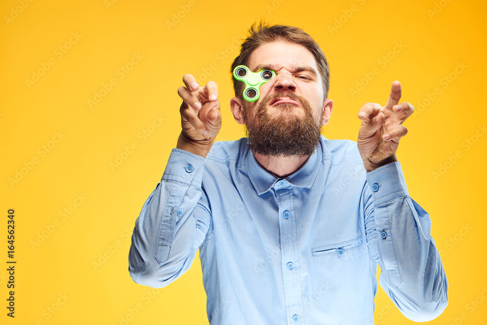 A young guy with a beard on a yellow background holds a spinner