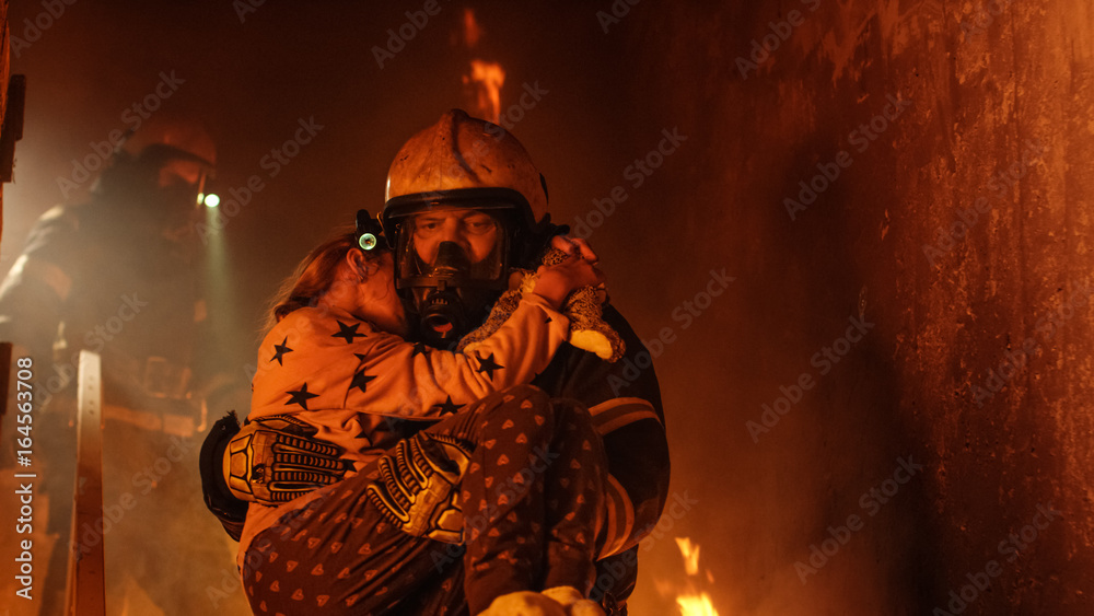 Fototapeta premium Brave Fireman Descends Stairs of a Burning Building and Holds Saved Girl in His Arms. Open fire and one Firefighter in the Background.