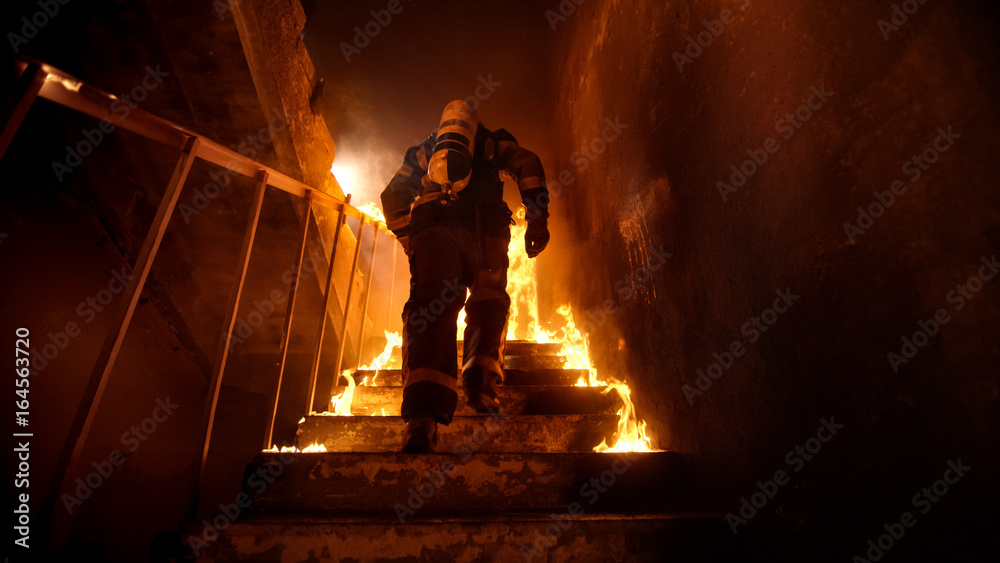 Obraz premium Strong and brave Firefighter Going Up The Stairs in Burning Building. Stairs Burn With Open Flames.