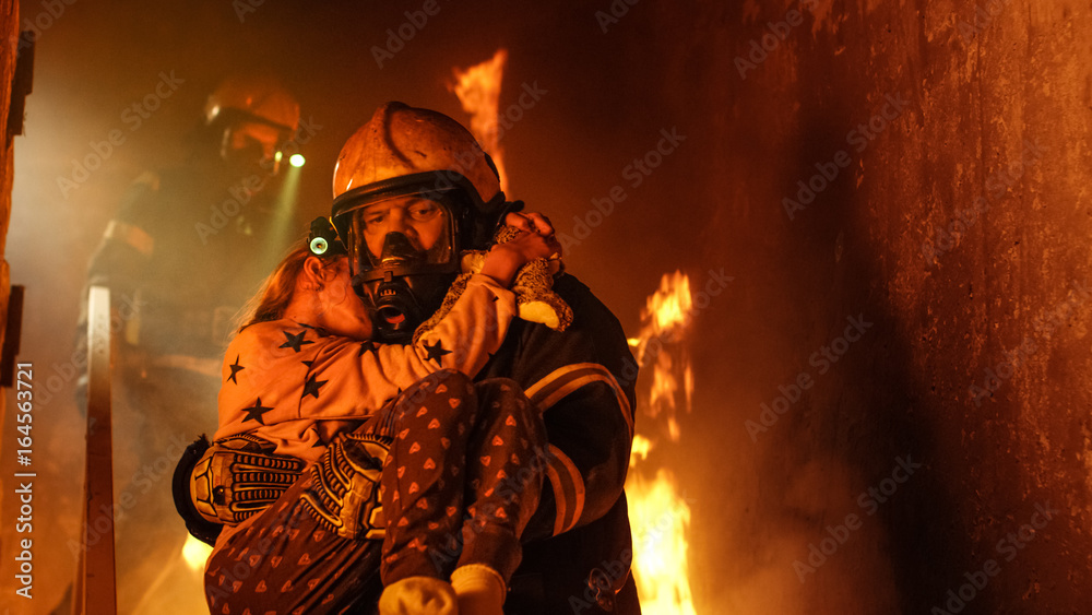 Naklejka premium Brave Fireman Descends Stairs of a Burning Building and Holds Saved Girl in His Arms. Open fire and one Firefighter in the Background.