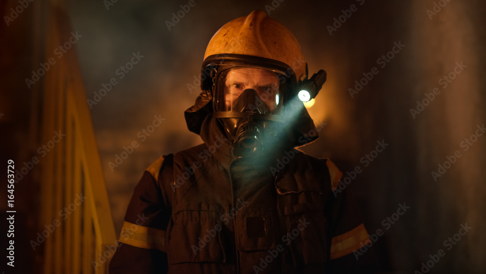 Fototapeta premium Portrait Shot of a Brave Fireman Standing in a Burning Building Fire Raging Behind Him. Open Flames and Smoke in the Background.