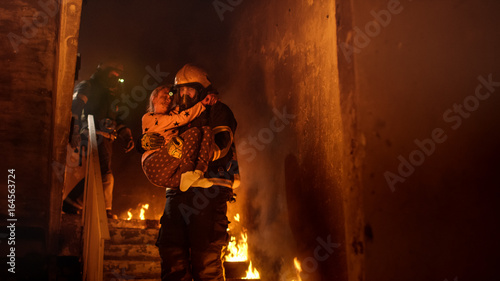 Brave Fireman Descends Stairs of a Burning Building with a Saved Girl in His Arms.