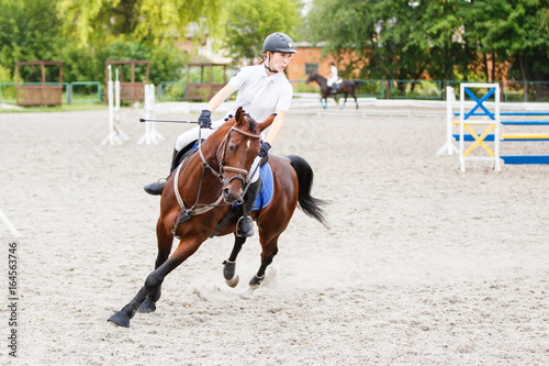 Young rider girl on bay horse galloping on her course at show jumping competition