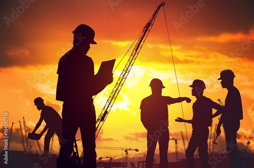 Silhouettes of workers working on construction site at suset.