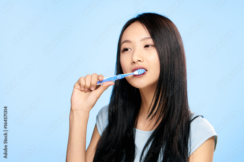 Young beautiful woman on a blue background brushes teeth, asian Young beautiful woman on a blue background brushes teeth, asian
