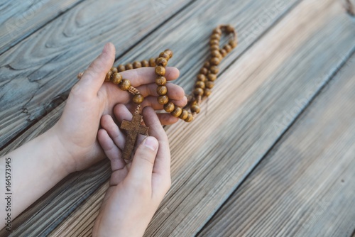Little boy holding old wooden rosary.