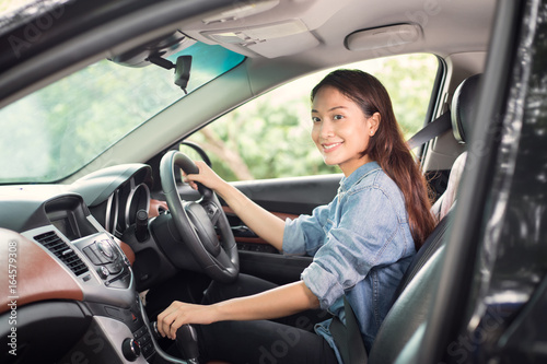 Beautiful Asian woman smiling and enjoying driving a car and hand is about to drive into gear on road for travel