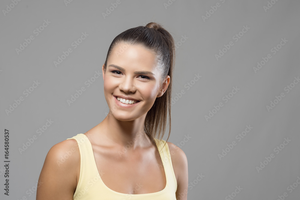 Cheerful excited sporty woman with perfect toothy smile looking at camera over gray studio background. Cheerful excited sporty woman with perfect toothy smile looking at camera over gray studio background.