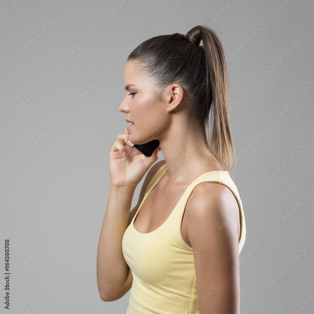 Profile side view of fit woman talking on the mobile phone looking down over gray studio background. Profile side view of fit woman talking on the mobile phone looking down over gray studio background.
