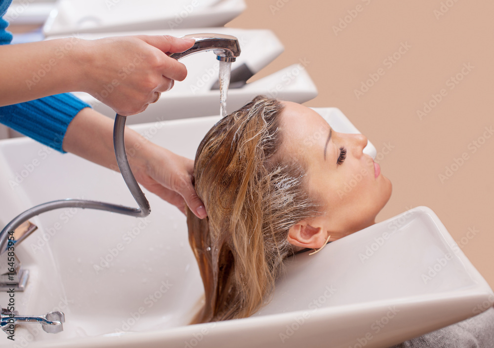 Naklejka premium Fryzjer zmywa szampon z włosów do młodej blondynki w salonie piękności.