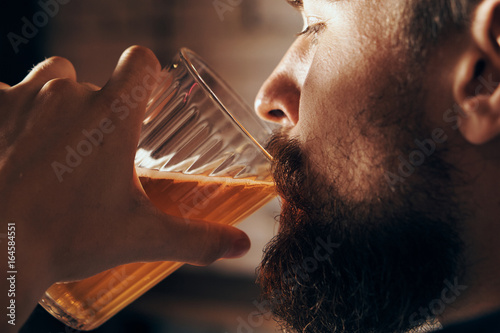A young guy with a beard drinks beer in a bar