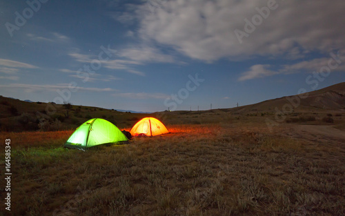 Green and red tent under the night sky in nature. The concept of traveling with tents