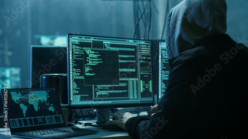 Dangerous Hooded Hacker Breaks into Government Data Servers and Infects Their System with a Virus. His Hideout Place has Dark Atmosphere, Multiple Displays, Cables Everywhere. photo