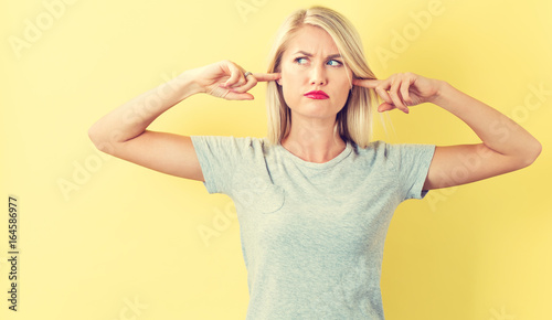 Young woman blocking her ears on a yellow background