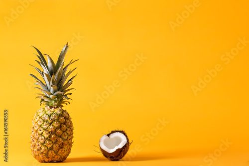 Whole pineapple and fresh coconut on a bright yellow background