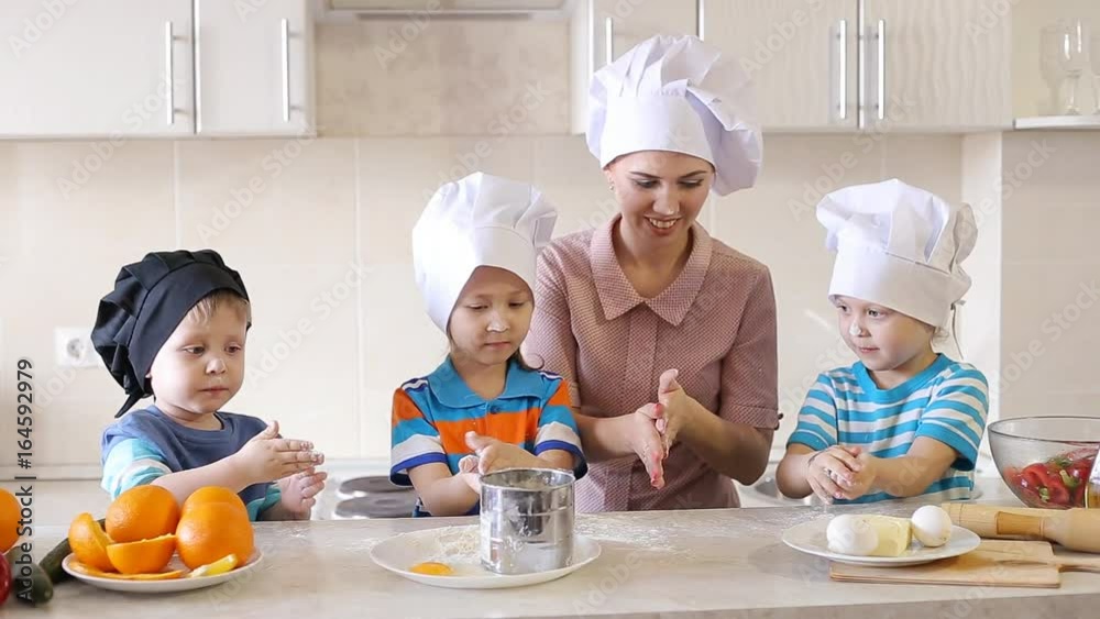 Young mother cooking in the kitchen with the children. Family having fun and preparing a meal. Young mother cooking in the kitchen with the children. Family having fun and preparing a meal.