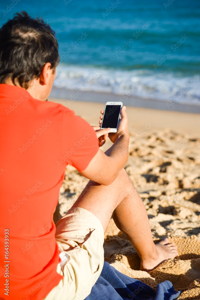 Tourist man looking using mobile phone on summer sand beach and sea outdoor background. Closeup of modern lifestyle holiday traveling season.