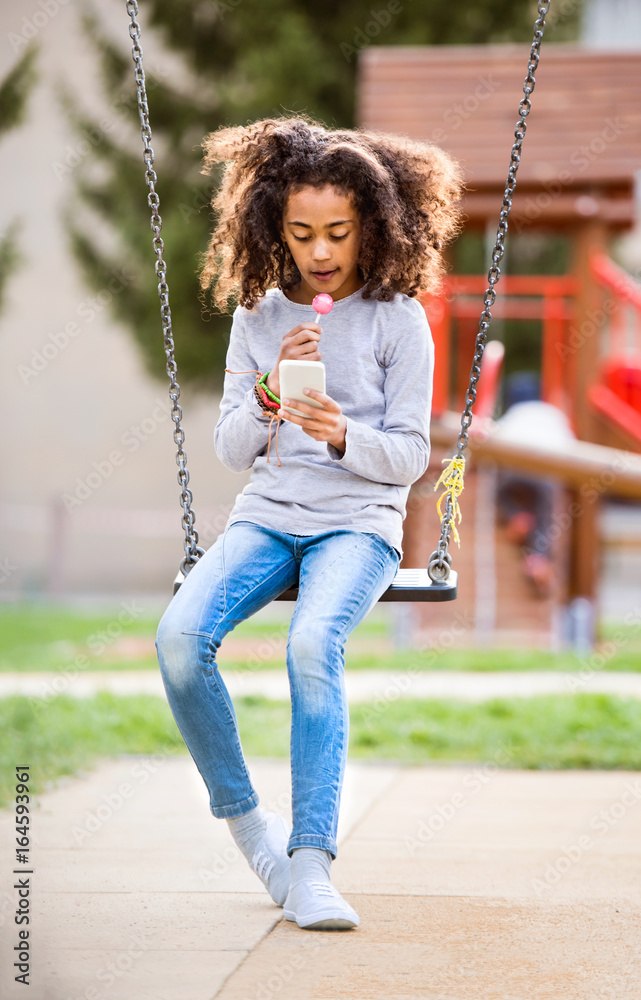African american girl on swing with smart phone texting. African american girl on swing with smart phone texting.