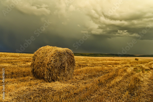 A round haystack on a cleared crooked field and a stormy sky. Beautiful landscape  space  hills in the background. After harvesting.  