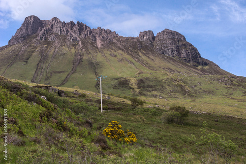 Assynt Peninsula, Scotland - June 7, 2012: Brown Mountain ridge along Loch Lurgainn under blue sky with a few white clouds. Green vegetation on foothills and lone electric pole and line. photo