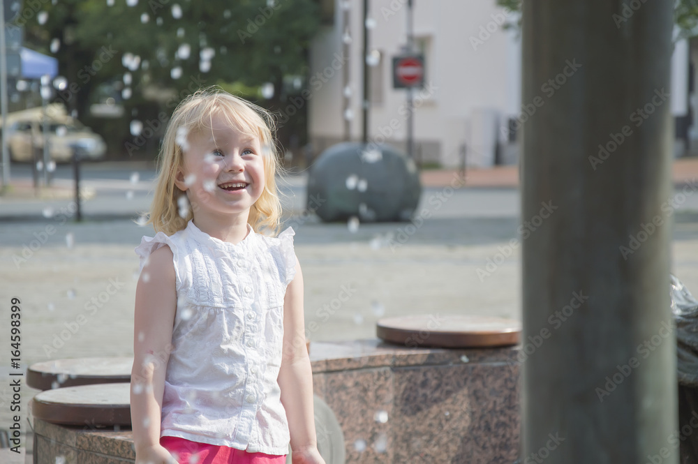 a little girl happily plays at the fountain in the summer hot season a little girl happily plays at the fountain in the summer hot season