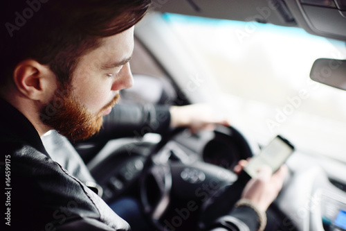 Young cute guy with a beard dials a message on the smartphone in the car © Evgeniy Kalinovskiy