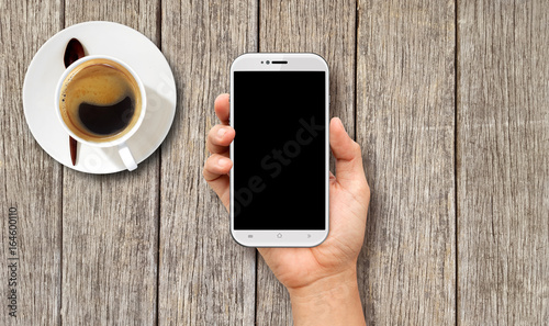 Hand holding White Smart phone on wood coffee table