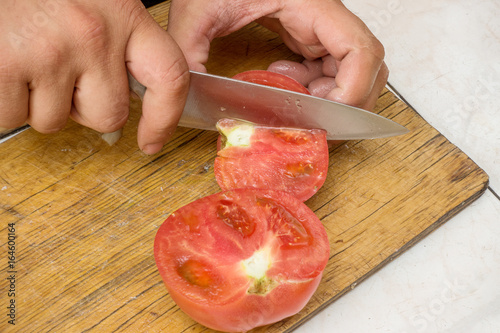 Slicing a ripe red tomato on a wooden cutting board