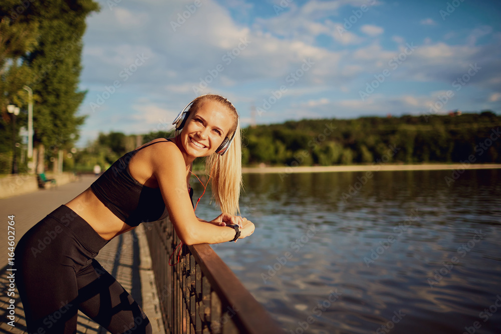 Young woman with headphones smiling at a lake in the park.