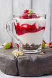 glass with raspberries, granola and yogurt arranged in layers closeup