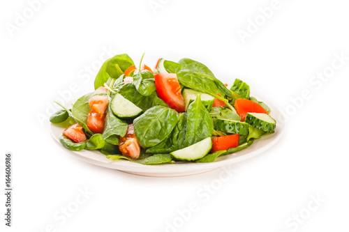 Salad with tomato, cucumber and spinach on the plate isolated on white background