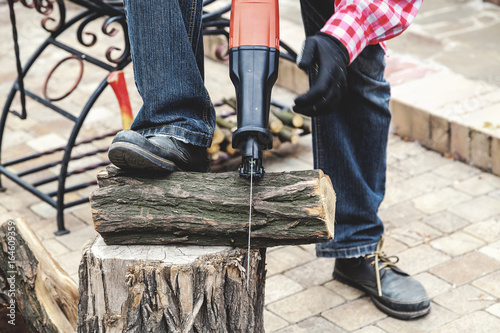 man in plaid shirt sawing piece of wood on stump
