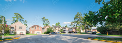 Suburban residential area, row of modern townhomes in Humble, Texas, US. Red brick houses surrounded with tall pine trees, cloud blue sky. Panorama view street intersection and multi-story townhouses. photo