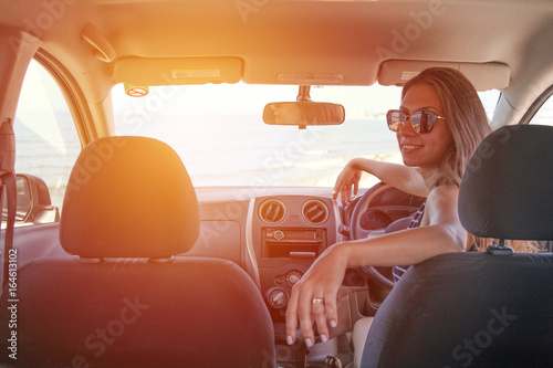 A woman sitting inside a rented car with a sea view