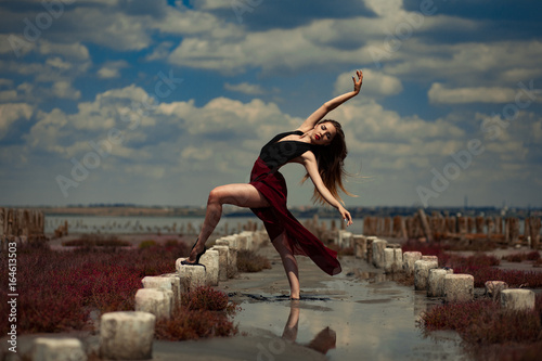 Ballerina is dancing in sand on beach and sky background.