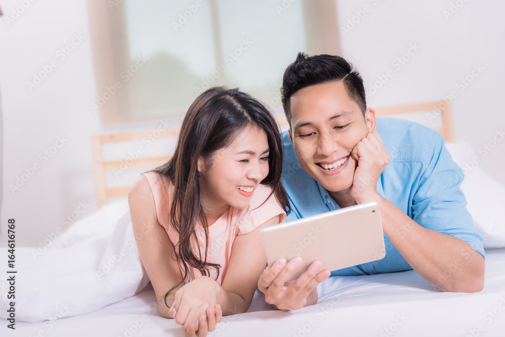 Happy Asian couple smile and enjoy while watching tablet in bed room. Happy Asian couple smile and enjoy while watching tablet in bed room.