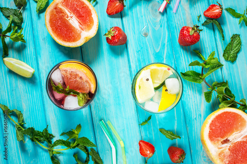 Glass of alcohol cold coctail decorated with ice, fruit and mint staying on wood table. Fresh juice on background with lemon, strawberry, lime