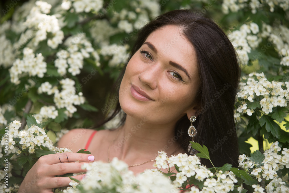 Beautiful brunette girl among blossoming flowers on a tree