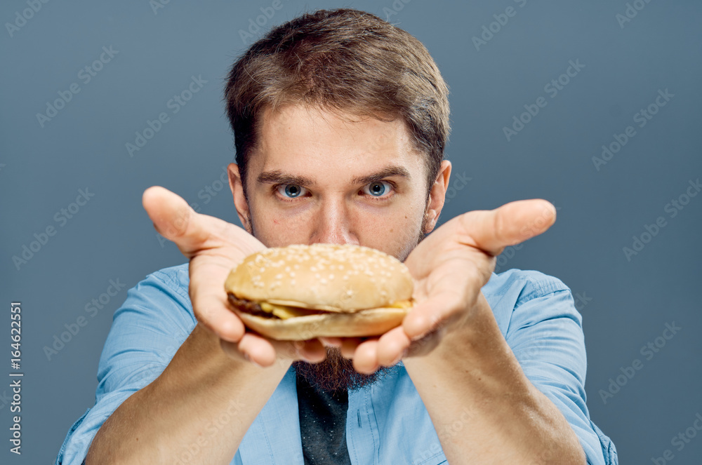 Young guy with a beard on a gray background holds a hamburger Young guy with a beard on a gray background holds a hamburger