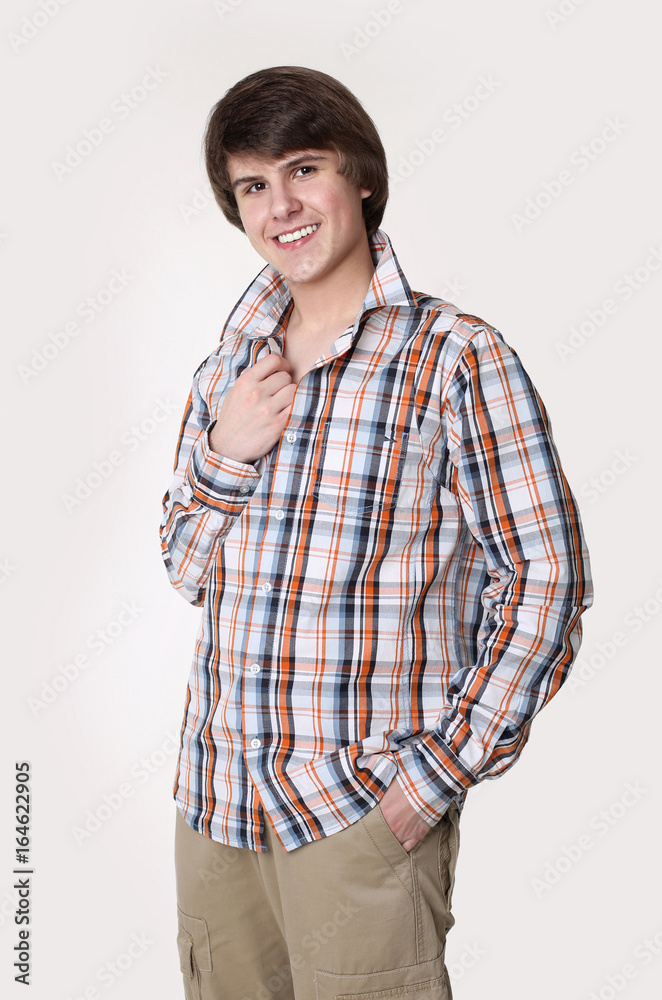Cheerful toothy young man in checked shirt and smart casual wear looking at camera and holding hands in pockets while standing isolated on studio white background Cheerful toothy young man in checked shirt and smart casual wear looking at camera and holding hands in pockets while standing isolated on studio white background